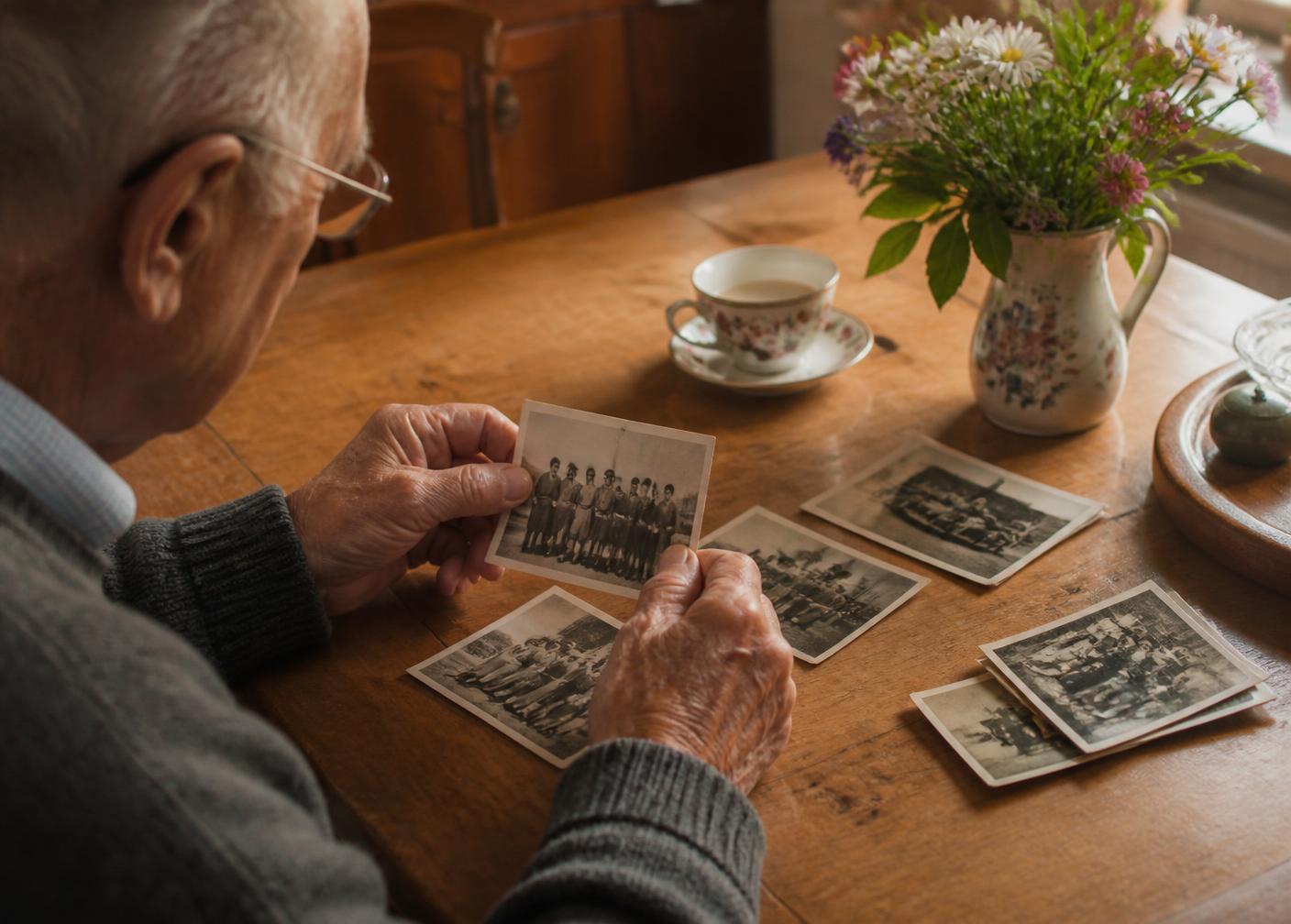 An older man looking through family photographs at a wooden kitchen table
